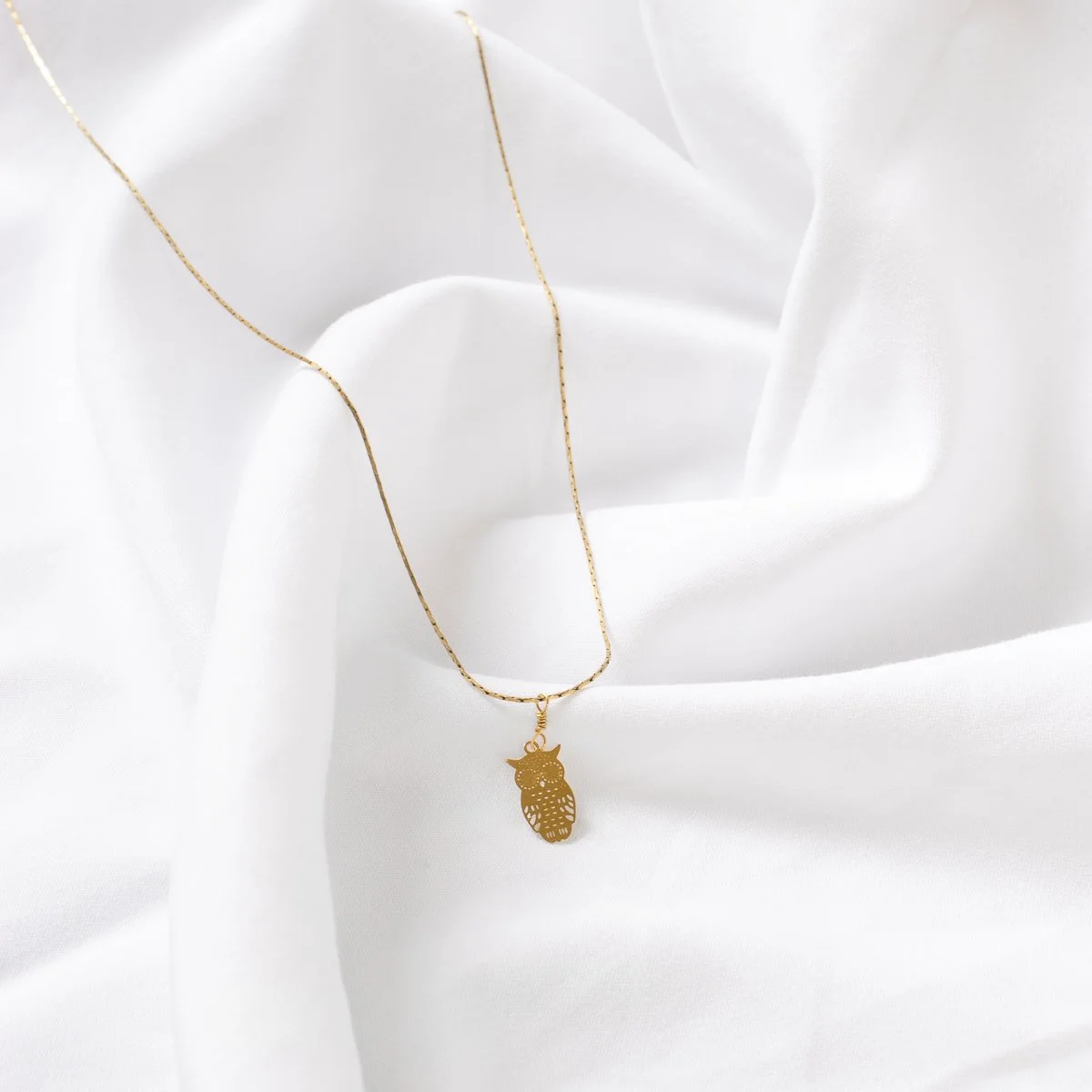Collier en or avec pendentif en forme de hibou, posé sur un tissu blanc