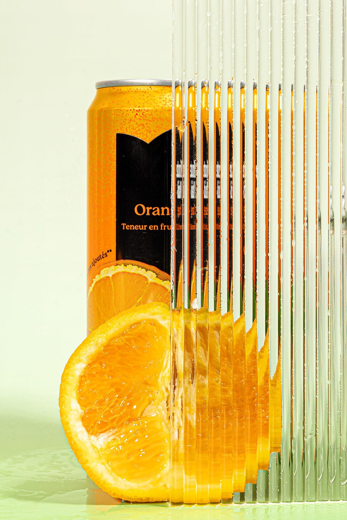 Une canette de jus d'orange à côté de tranches d'orange, avec un effet de déchirure verticale dans l'image.