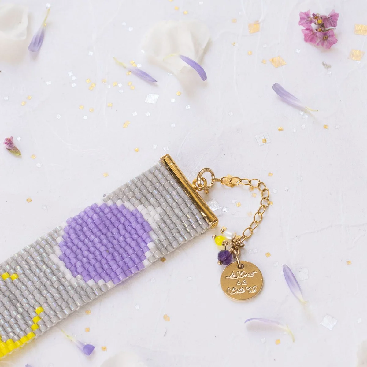 Un porte-clés en perles avec un design de pinceau et un message en français gravé, posé sur une surface blanche avec des fleurs et des confettis.