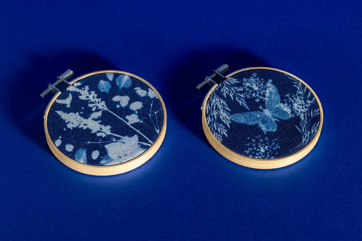 Deux cerceaux à broder avec des motifs floraux et un papillon en perles sur un fond bleu.