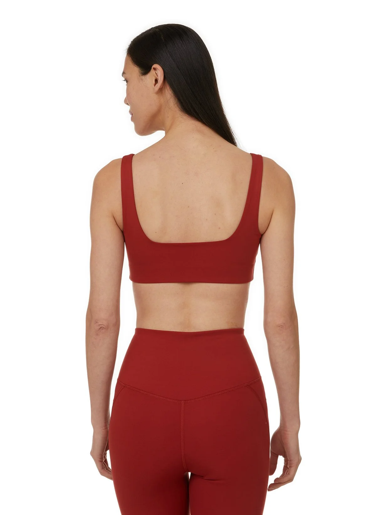 Une femme vue de dos, portant un top rouge sans manches et un legging rouge, avec des cheveux longs noirs.