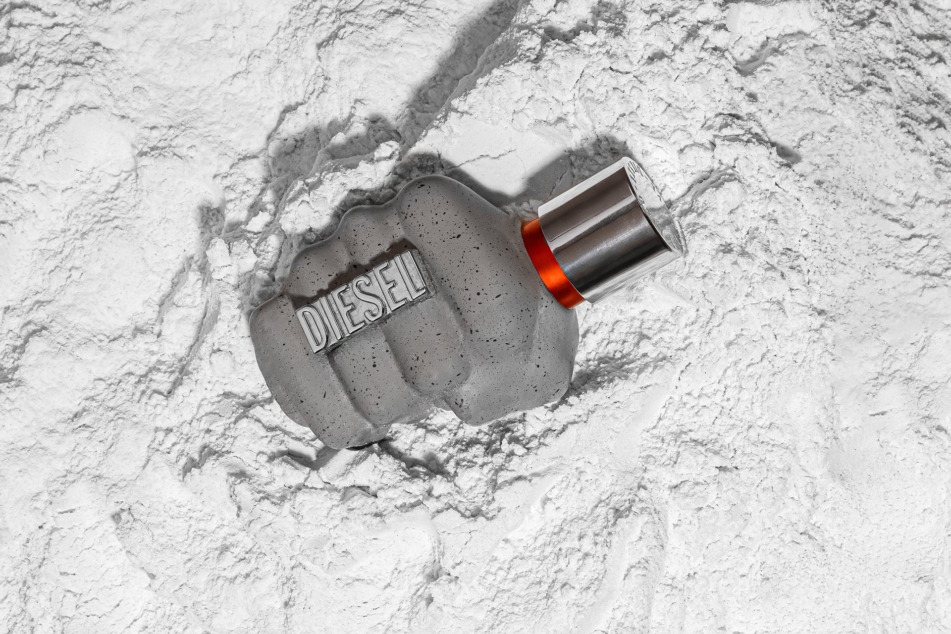 Un flacon de parfum Diesel posé sur de la poudre blanche, probablement du talc ou de la farine, dans un décor blanc.