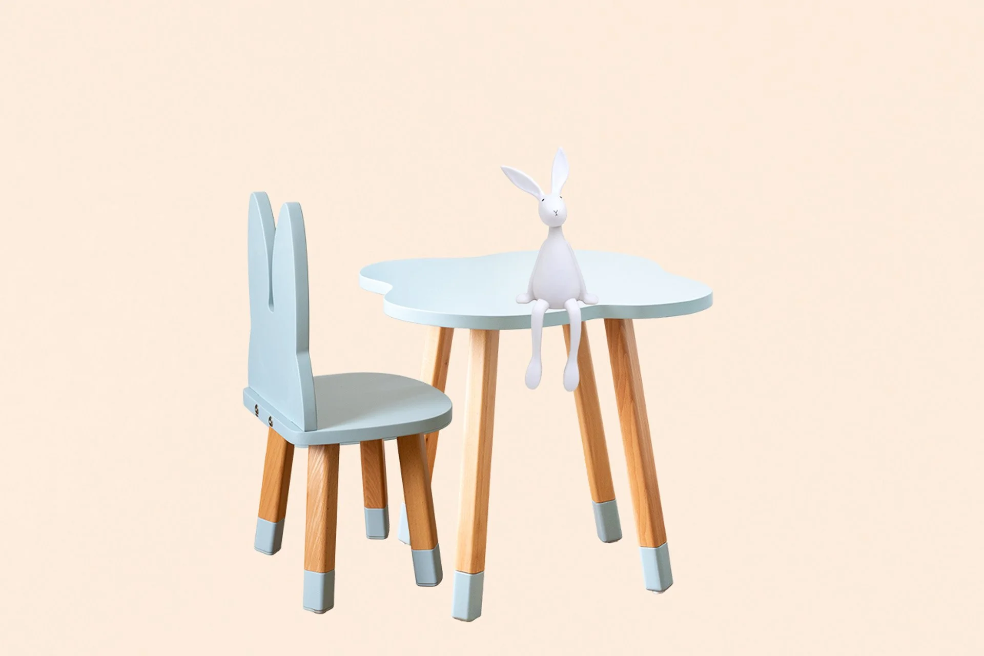 Une petite table avec des jambes en bois et une moquette blanche, accompagnée d'une chaise en bois avec un dos en forme de lapin, et un lapin blanc en plastique assis au centre de la table contre un fond beige clair.