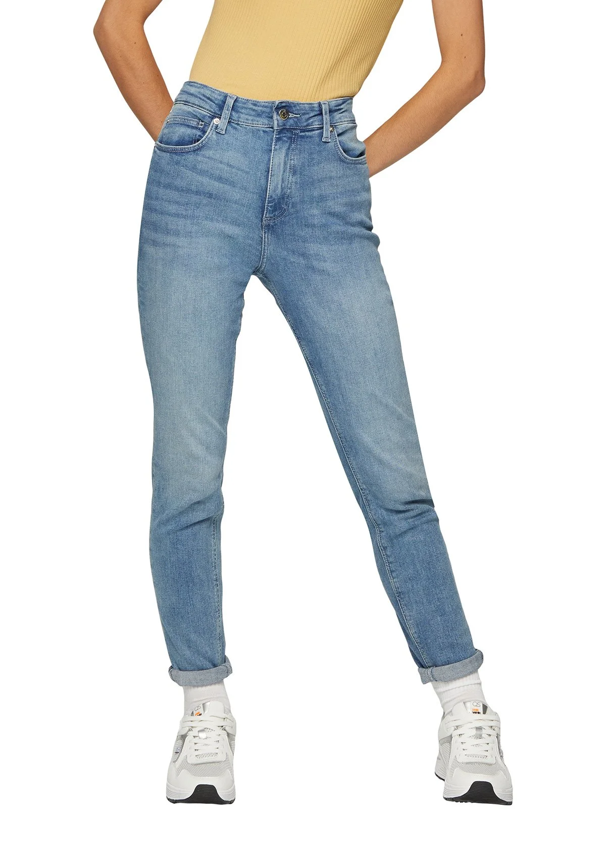 Jeune femme portant un jean bleu clair, une veste jaune, et des baskets blanches.