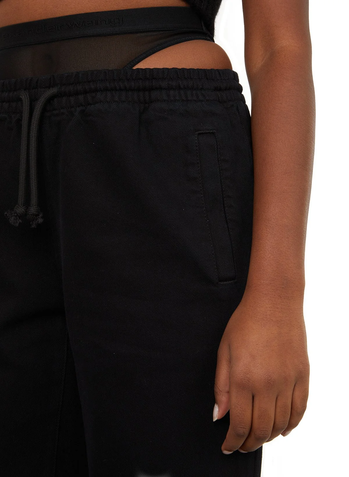 Vêtements de sport noirs, comprenant un pantalon avec une poche latérale et un haut en tissu mesh transparent.