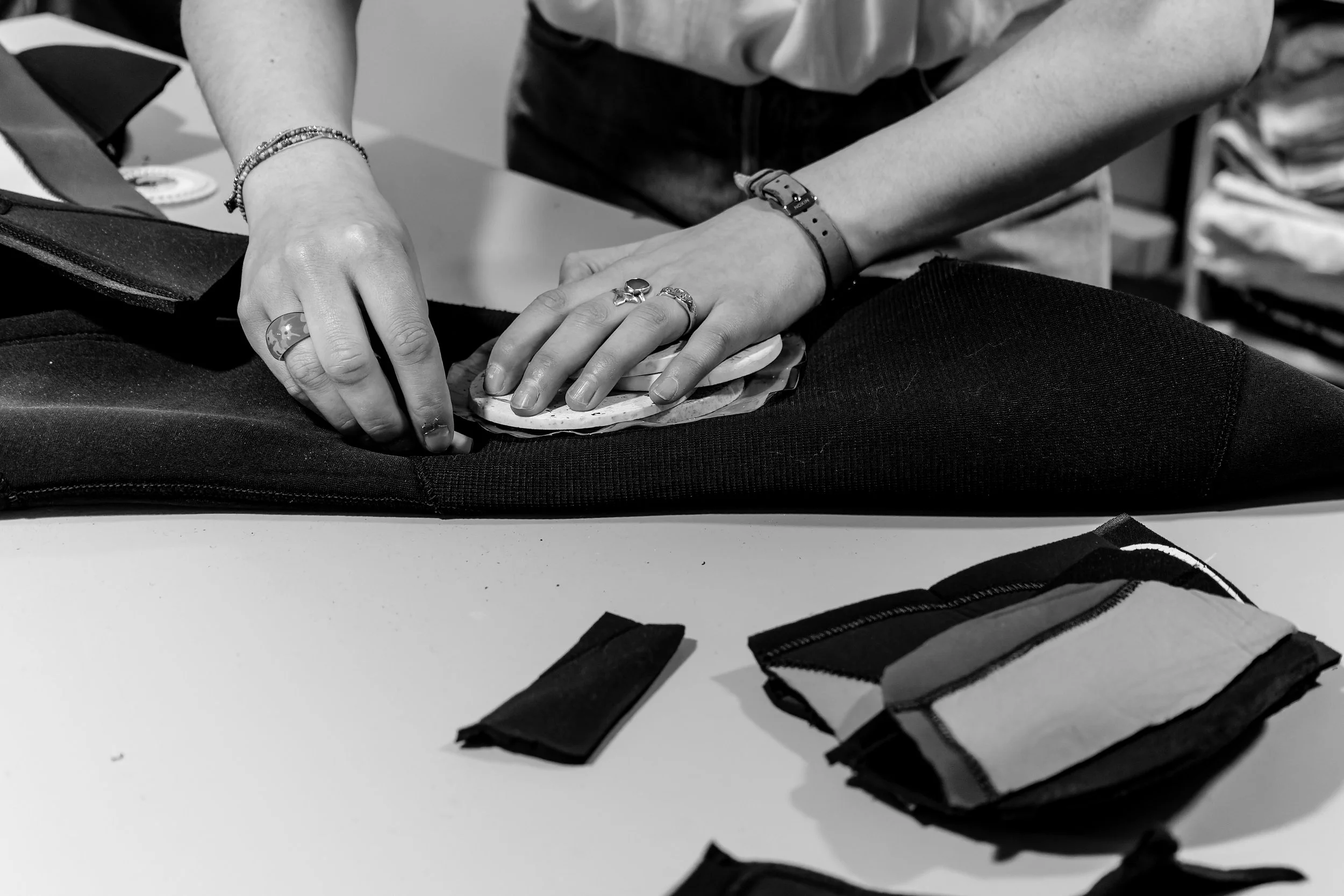 Une personne met un tissu dans une housse de protection noire, des échantillons de tissu sont posés sur une table. La personne porte plusieurs bijoux et un bracelet.