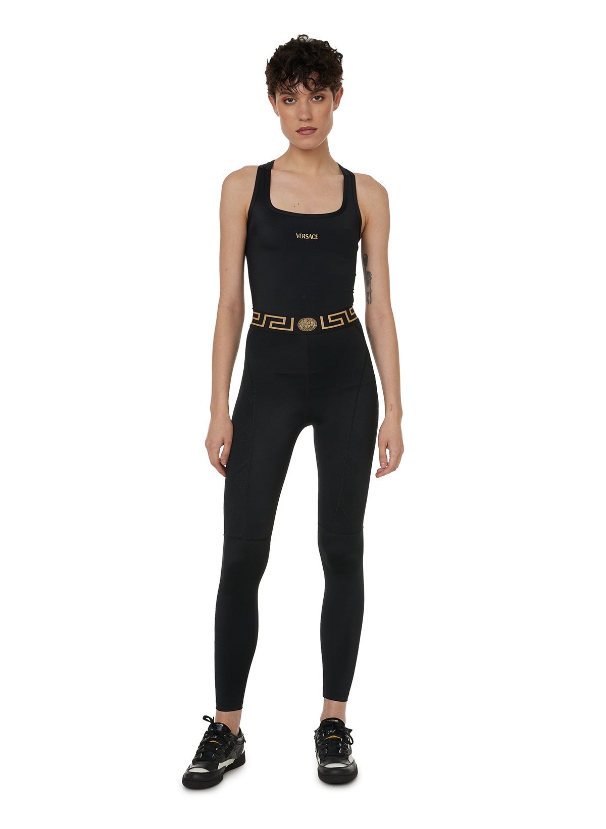 Une femme porte un haut noir, un pantalon de sport noir et des baskets noires et blanches.