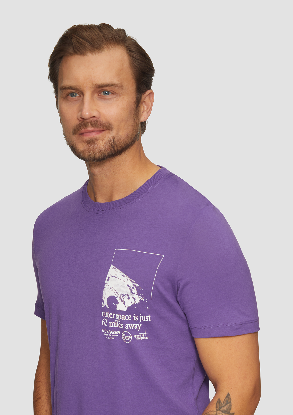 Homme portant un t-shirt violet avec un motif de l'espace et un texte en anglais.