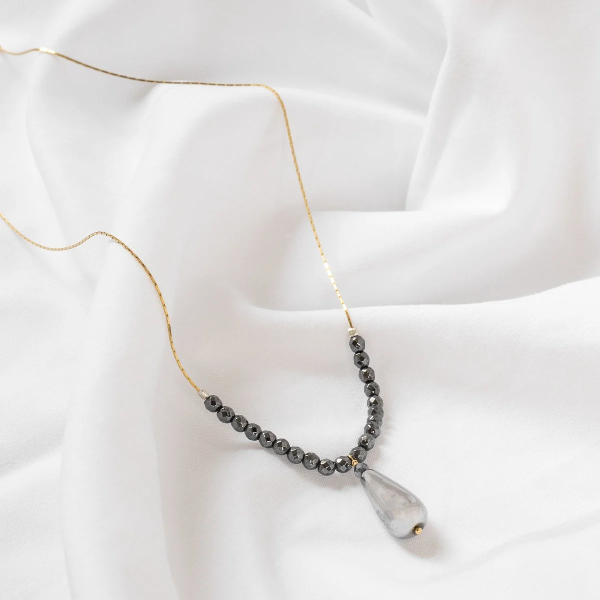 Collier délicat avec perles noires et pendentif en forme de goutte d'eau en pierre translucide, posé sur un tissu blanc