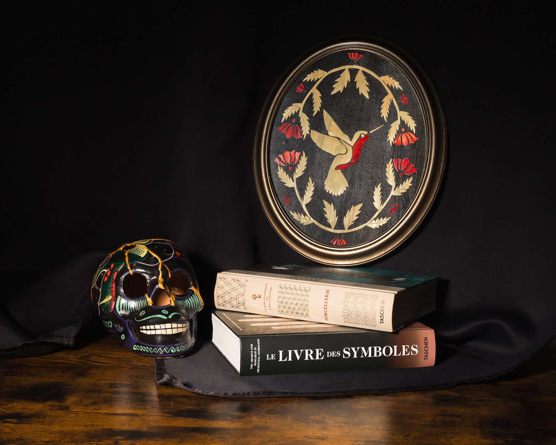 Objet décoratif avec un coq, livres, un masque coloré, tous sur une surface en bois et un fond noir.