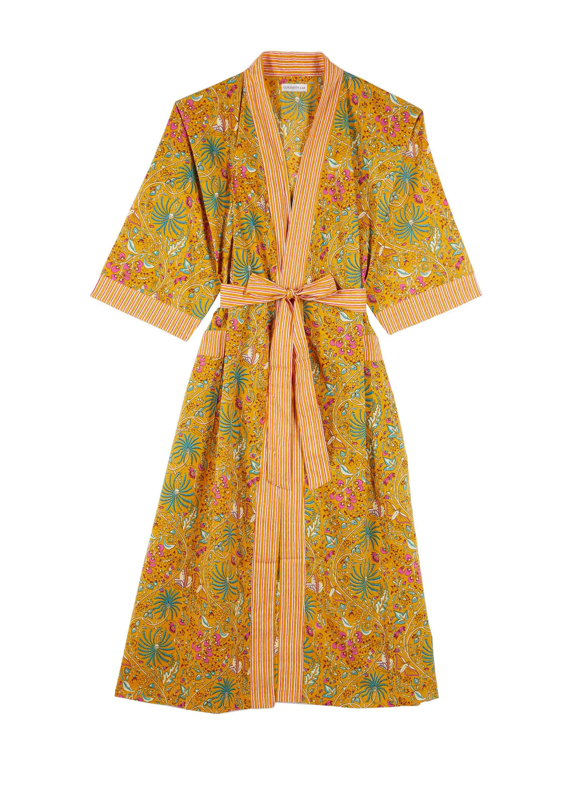 Robe longue à motifs floraux jaunes, roses, et vert avec un col V et une ceinture rayée orange, jaune, et blanc.