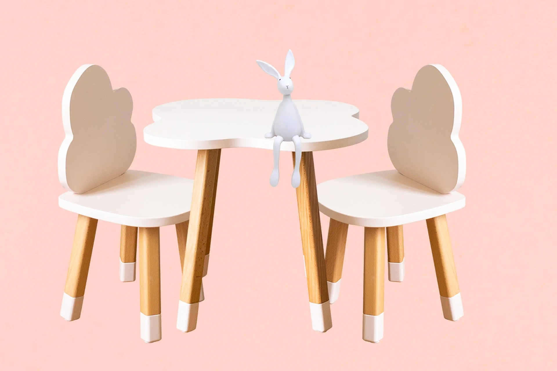 Table pour enfants avec deux chaises blanches en forme de nuages et un lapin en plastique blanc assis au centre, contre un fond rose pastel.