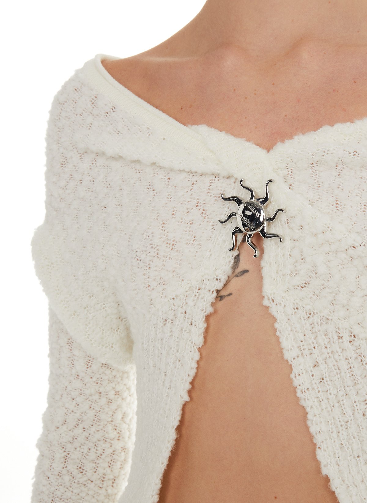 Femme portant une épaulette en laine blanche avec une broche en forme de crabe en métal argenté.