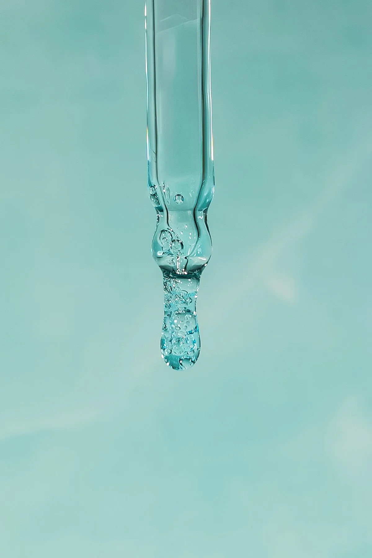 Goutte d'eau suspendue avec des bulles d'air à l'intérieur, en suspension contre un fond bleu clair.