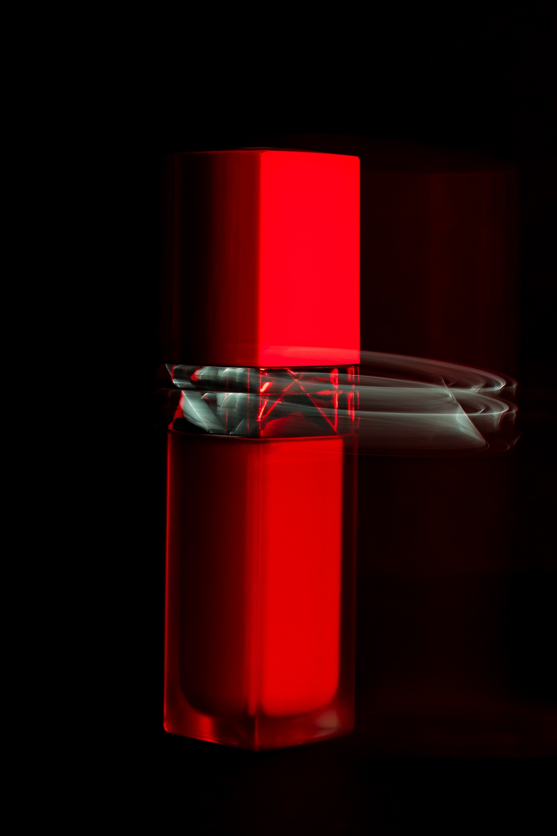 Structure luminescente rouge avec effets de lumière, reflété sur une surface noire.