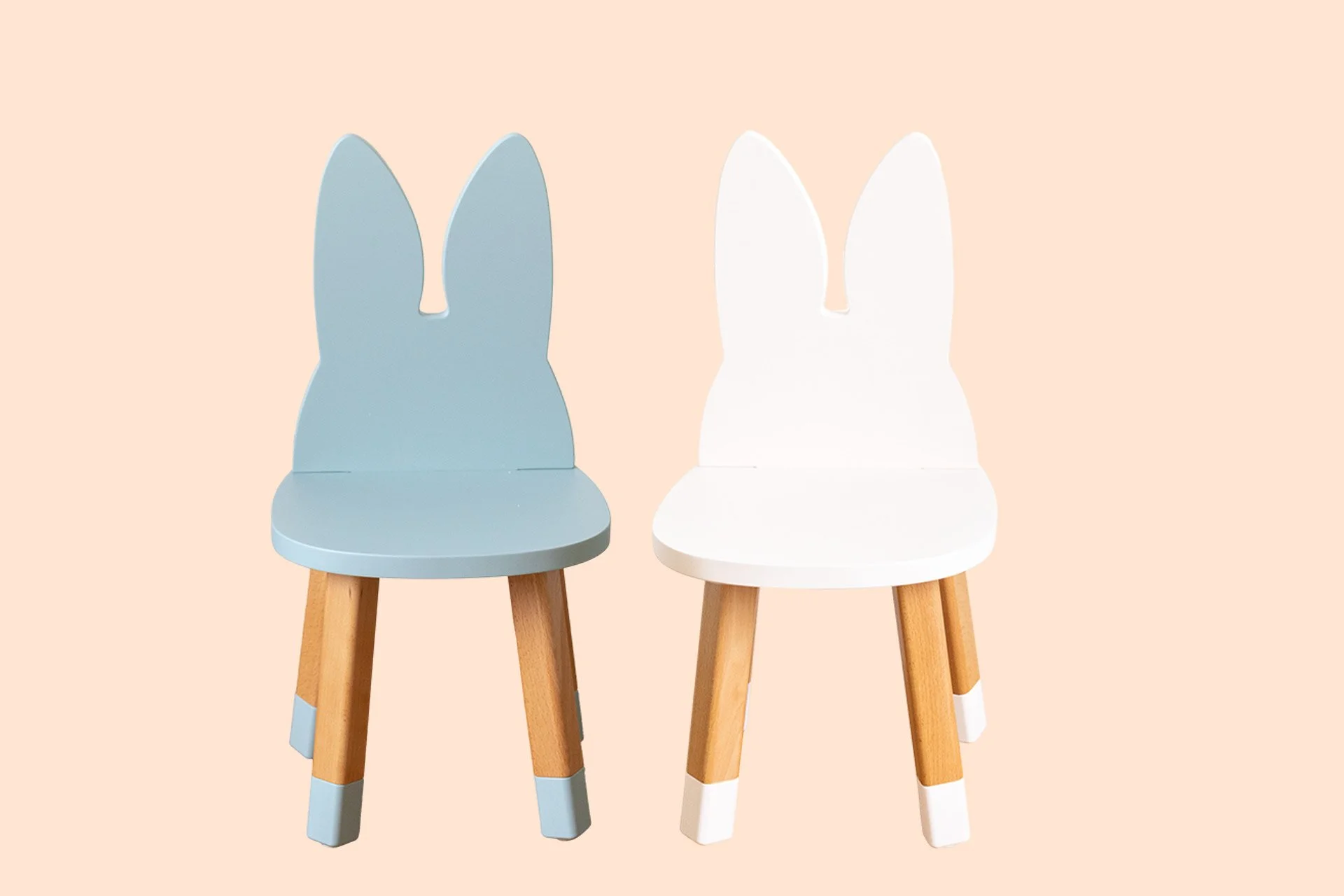 Deux chaises pour enfants en forme de lapin, une en bleu et l'autre en blanc, avec des jambes en bois clair et des extrémités peintes en gris et blanc, contre un fond beige.