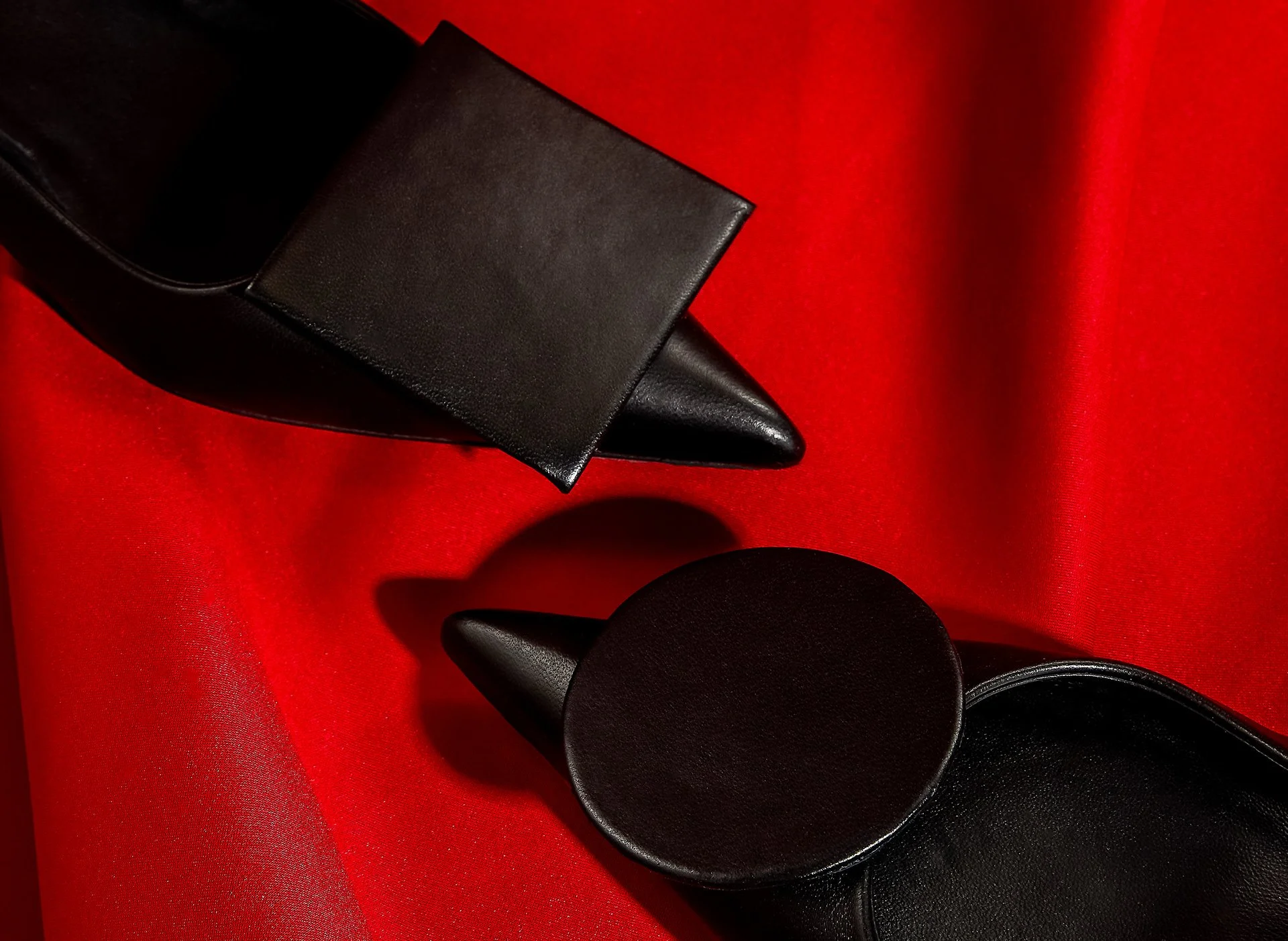 Chaussures noires en cuir, bout pointu, posées sur un fond rouge satinée.