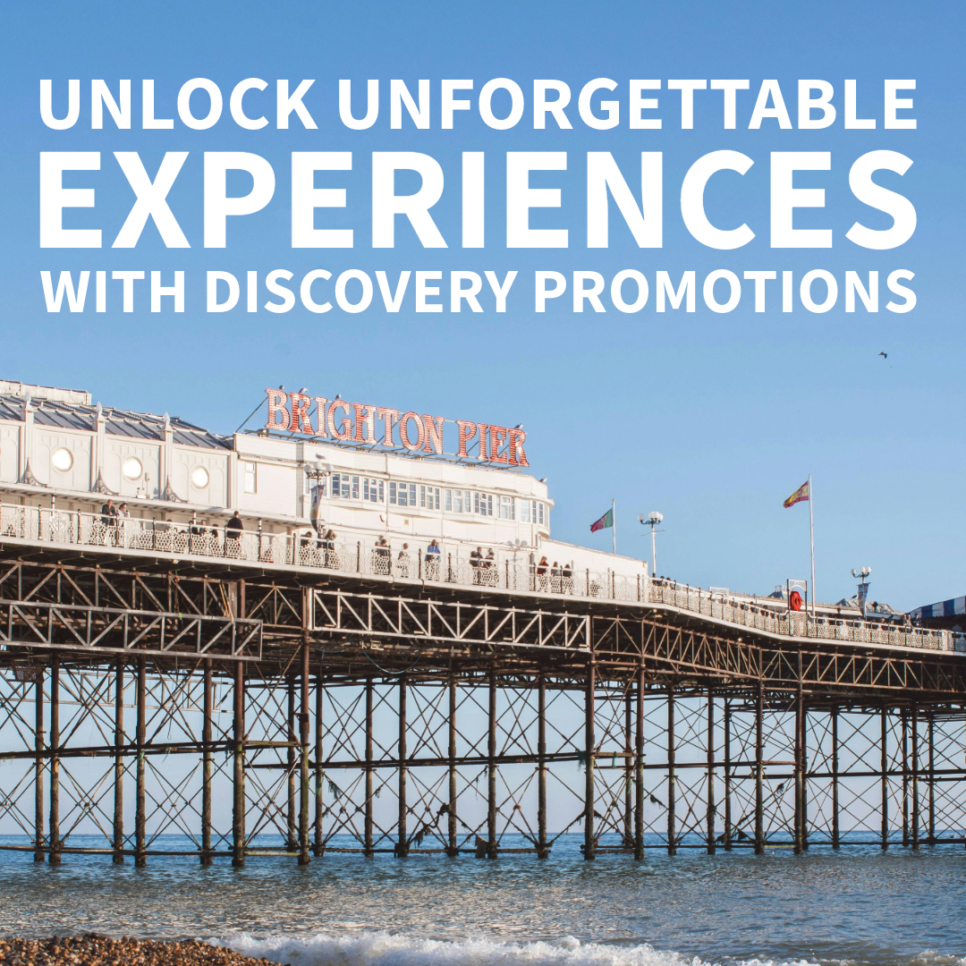 Une vue de la jetée de Brighton avec le nom lumineux 'Brighton Pier', un ciel bleu clair, et des gens se promenant sur la plateforme en bois au-dessus de l'eau. Texte superposé : 'Unlock Unforgettable Experiences with Discovery Promotions'.