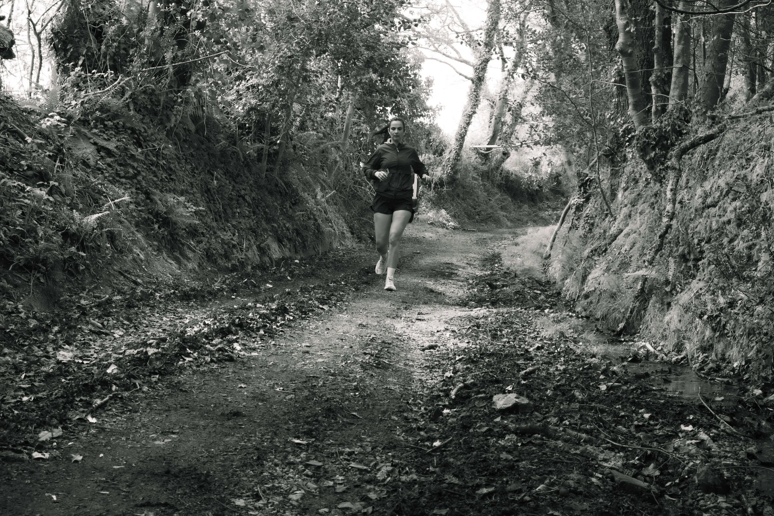 Une femme court sur un sentier de forêt en noir et blanc.