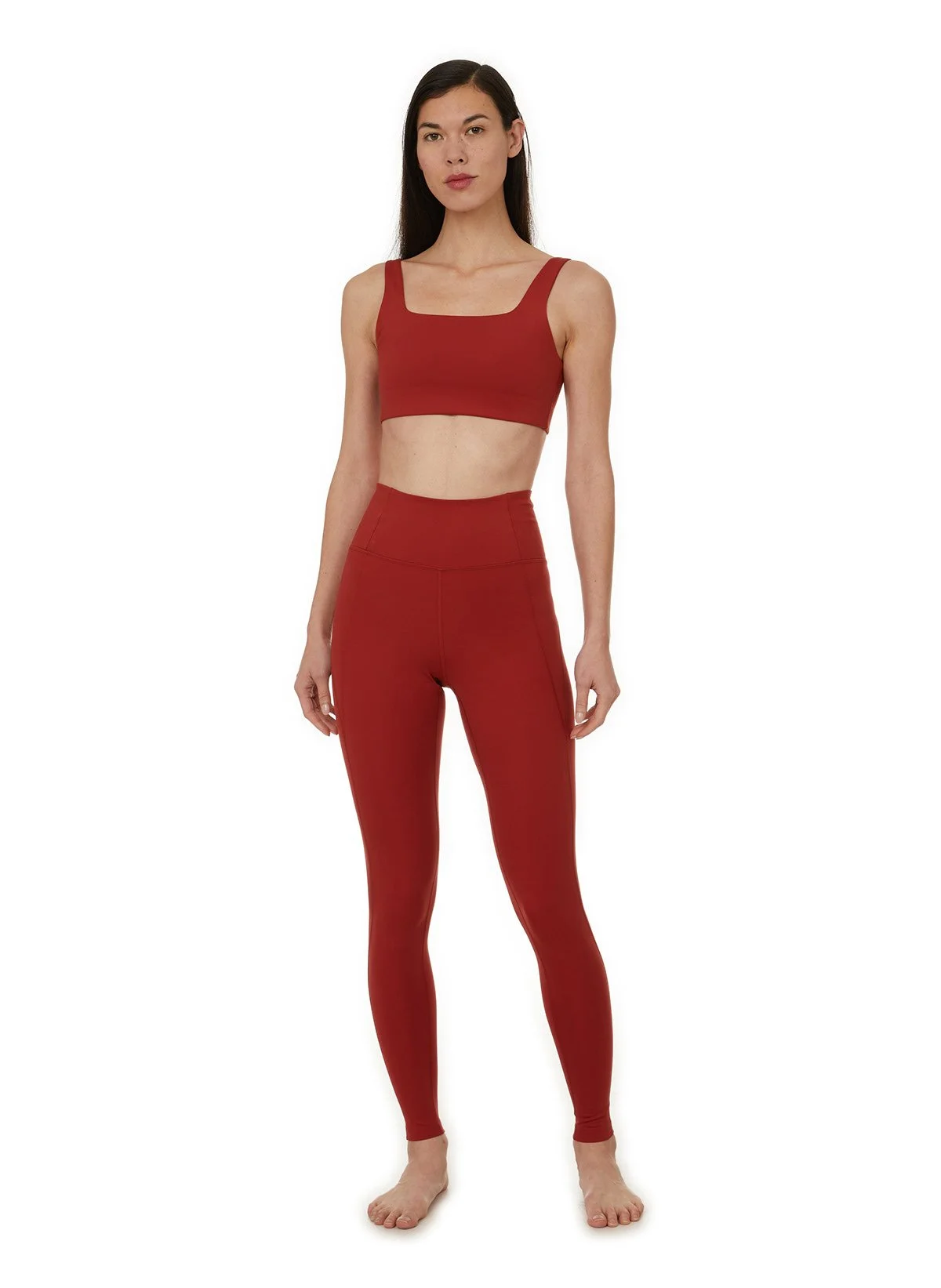 Femme portant un ensemble de vêtements de sport rouge, comprenant un haut crop top et un legging, debout contre un fond blanc.