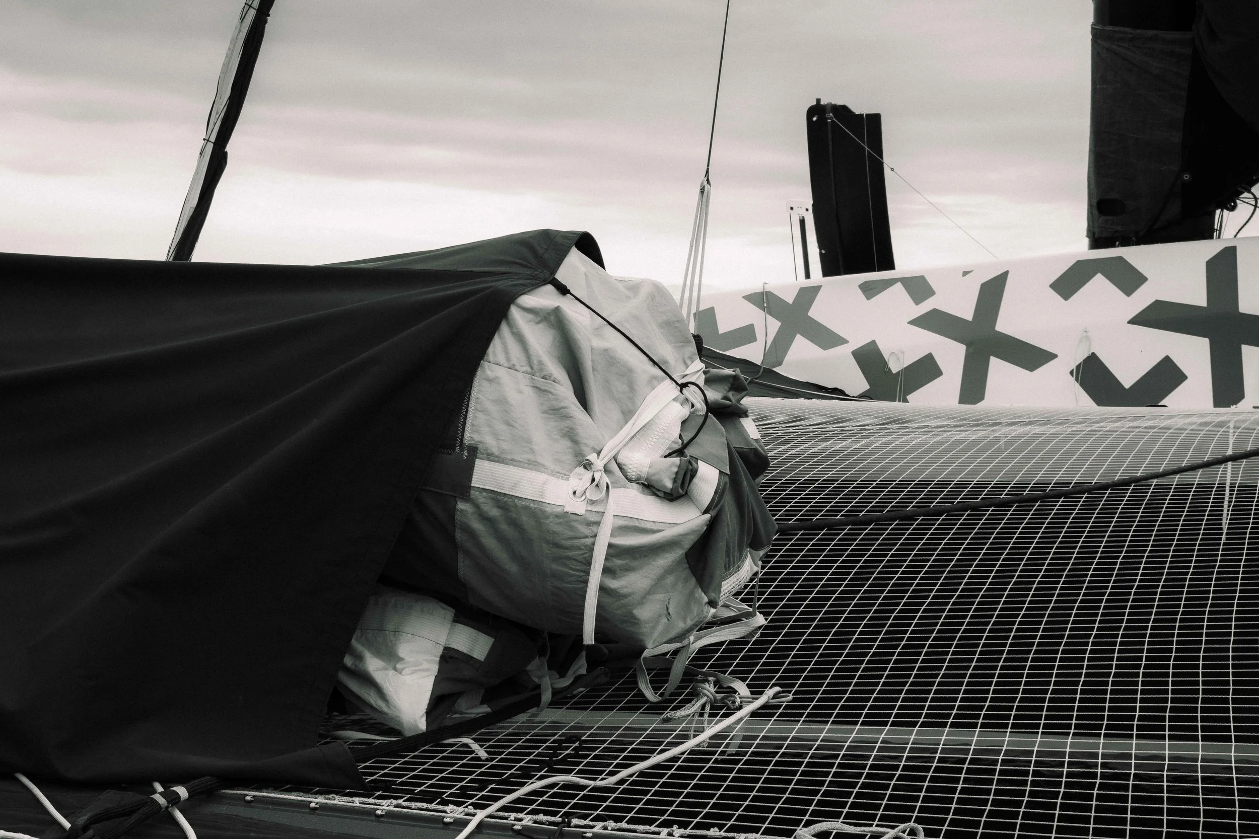 Détails d'une voile de bateau de course avec des cordages et un sac de rangement sur le pont.