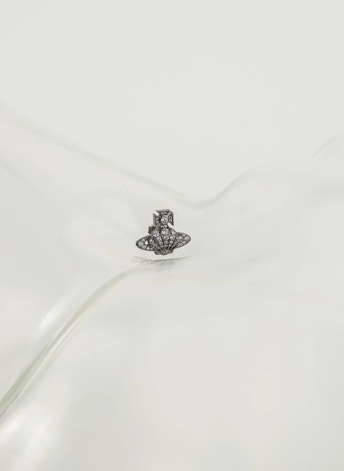 Une boucle d'oreille en forme d'un symbole avec des pierres brillantes, posée sur un fond blanc.