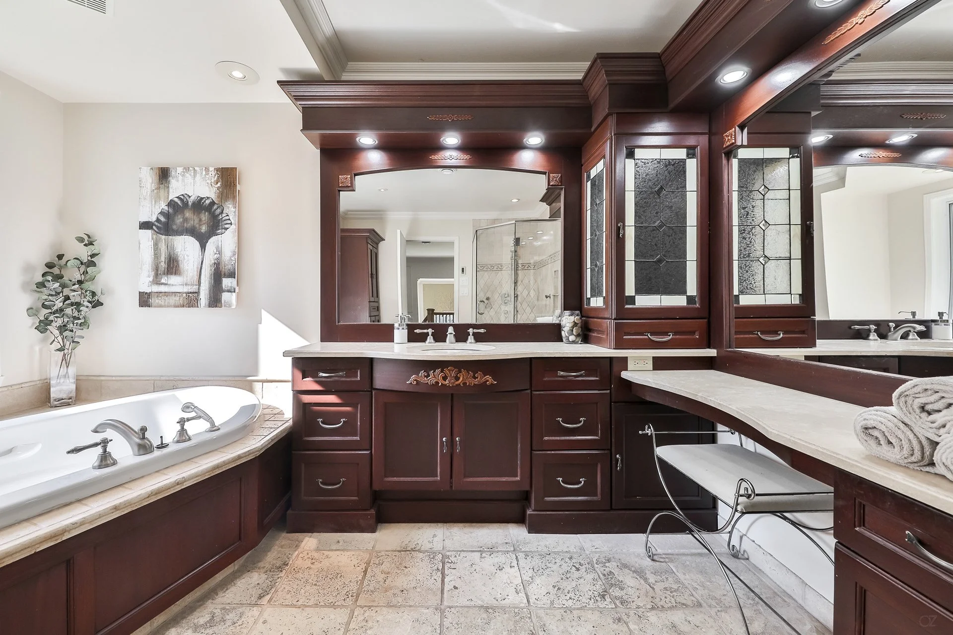 Salle de bain avec baignoire et grand miroir au mur, armoires en bois foncé, comptoir en pierre, rouleaux de serviettes et décor mural floral