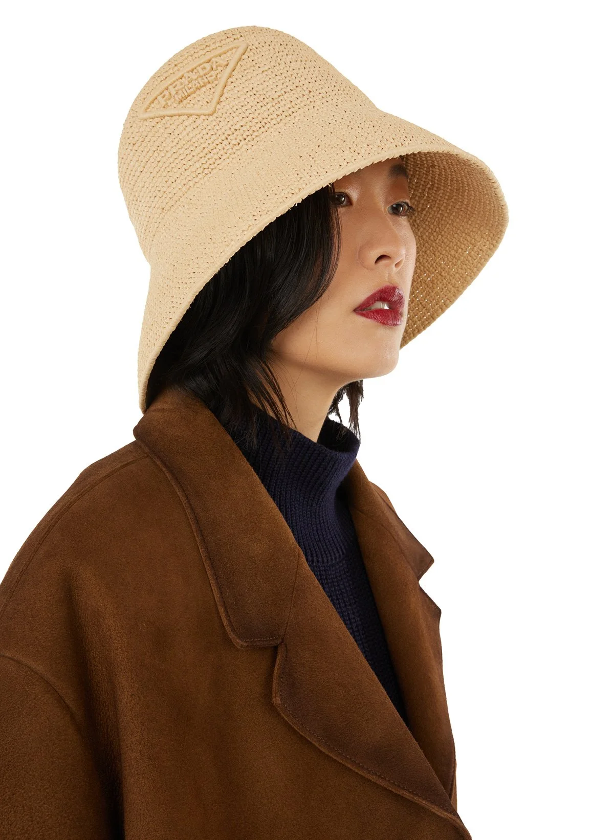 Femme portant un chapeau en crochet beige, une veste marron et un pull noir, regardant vers la droite.