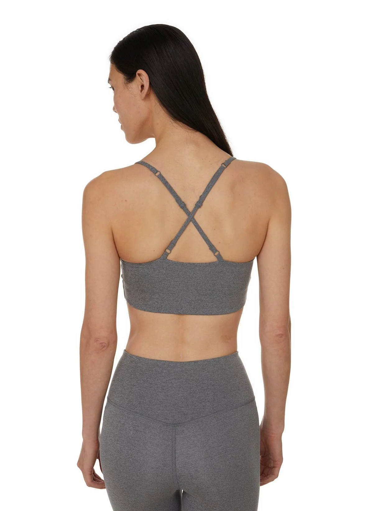 Femme portant un haut de sport gris avec bretelles croisées dans le dos, vue de dos, portant un pantalon de sport gris.