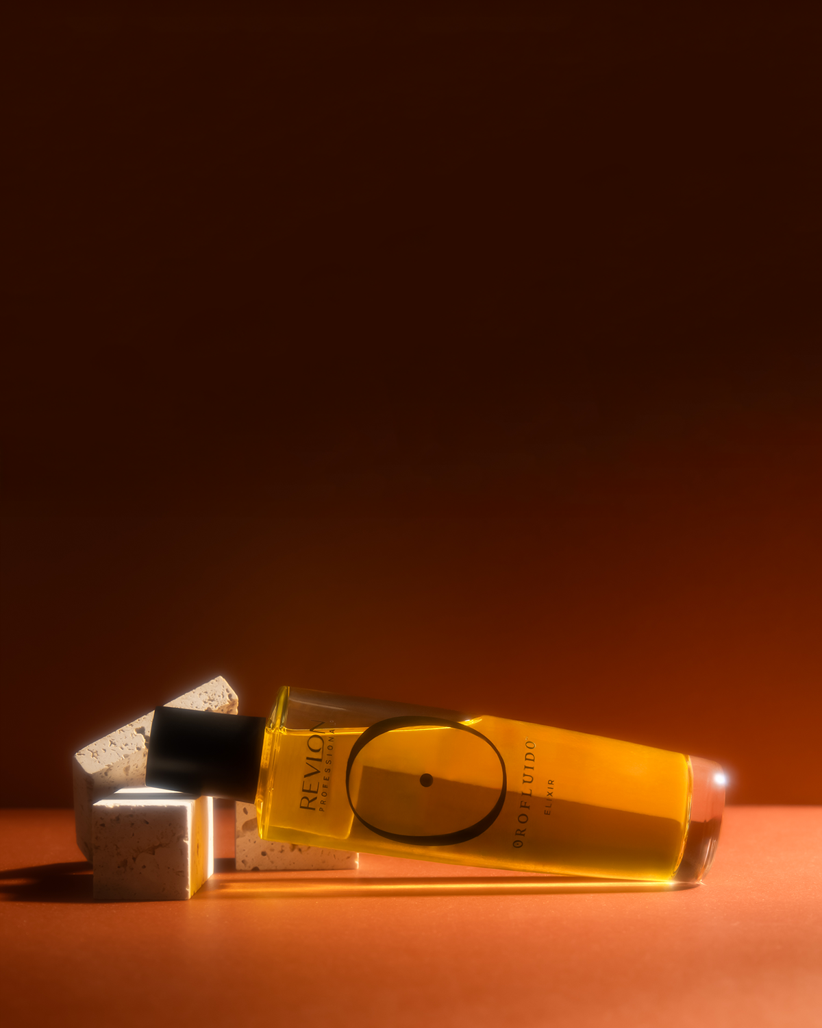 Flacon d'huile parfumée Revlon Professionnel avec des blocs en pierre blanche et un éclairage chaud.
