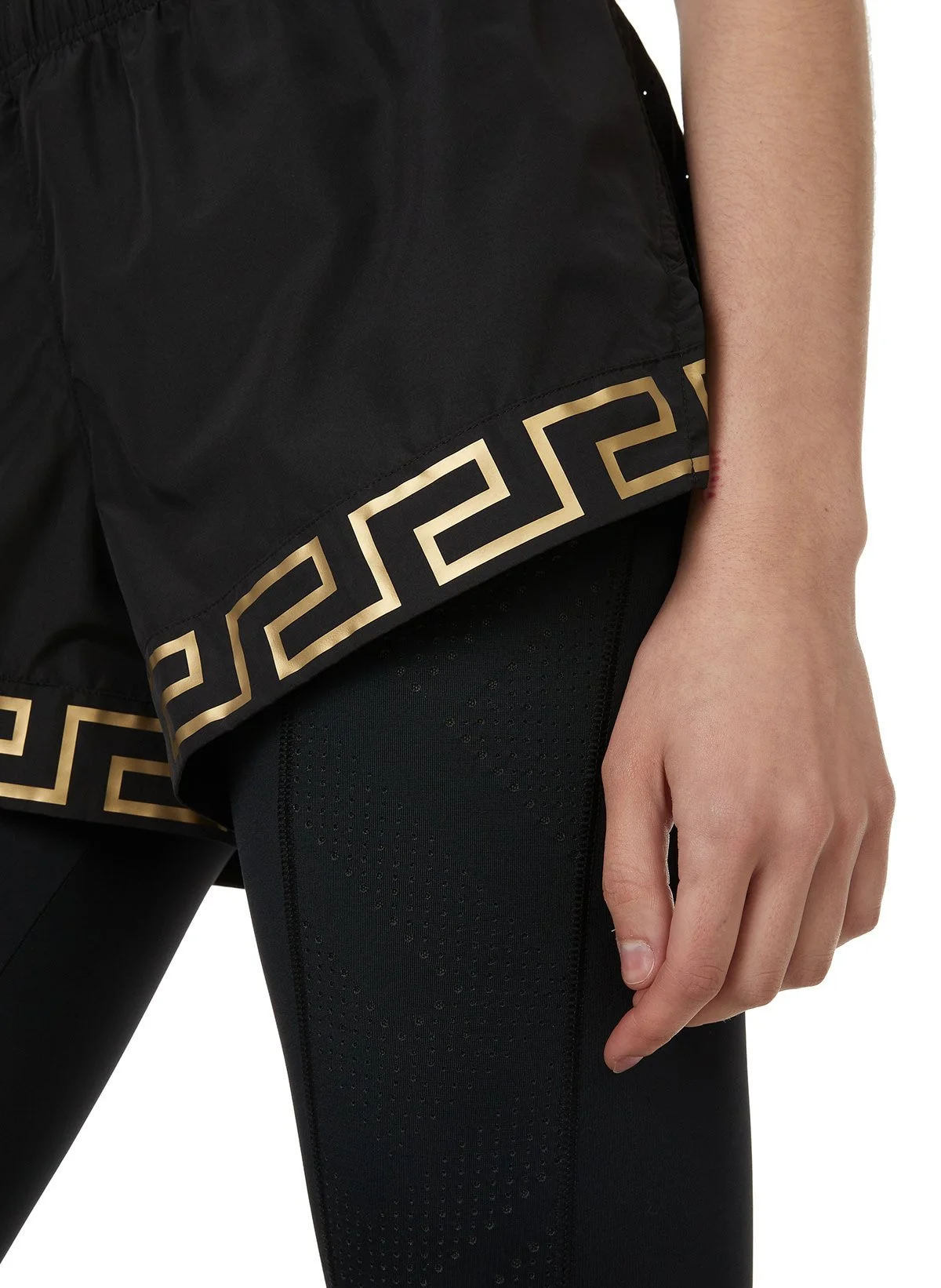 Close-up de la jambe et de la main d'une personne portant un short noir avec un ourlet doré à motif grec ancien.