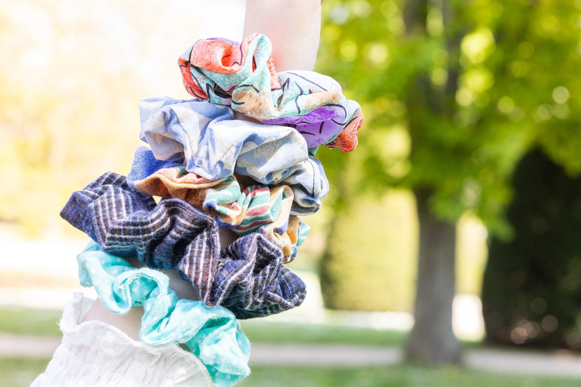 Une main tient une multitude d'élastiques à cheveux de différentes couleurs et motifs, avec un parc en arrière-plan.