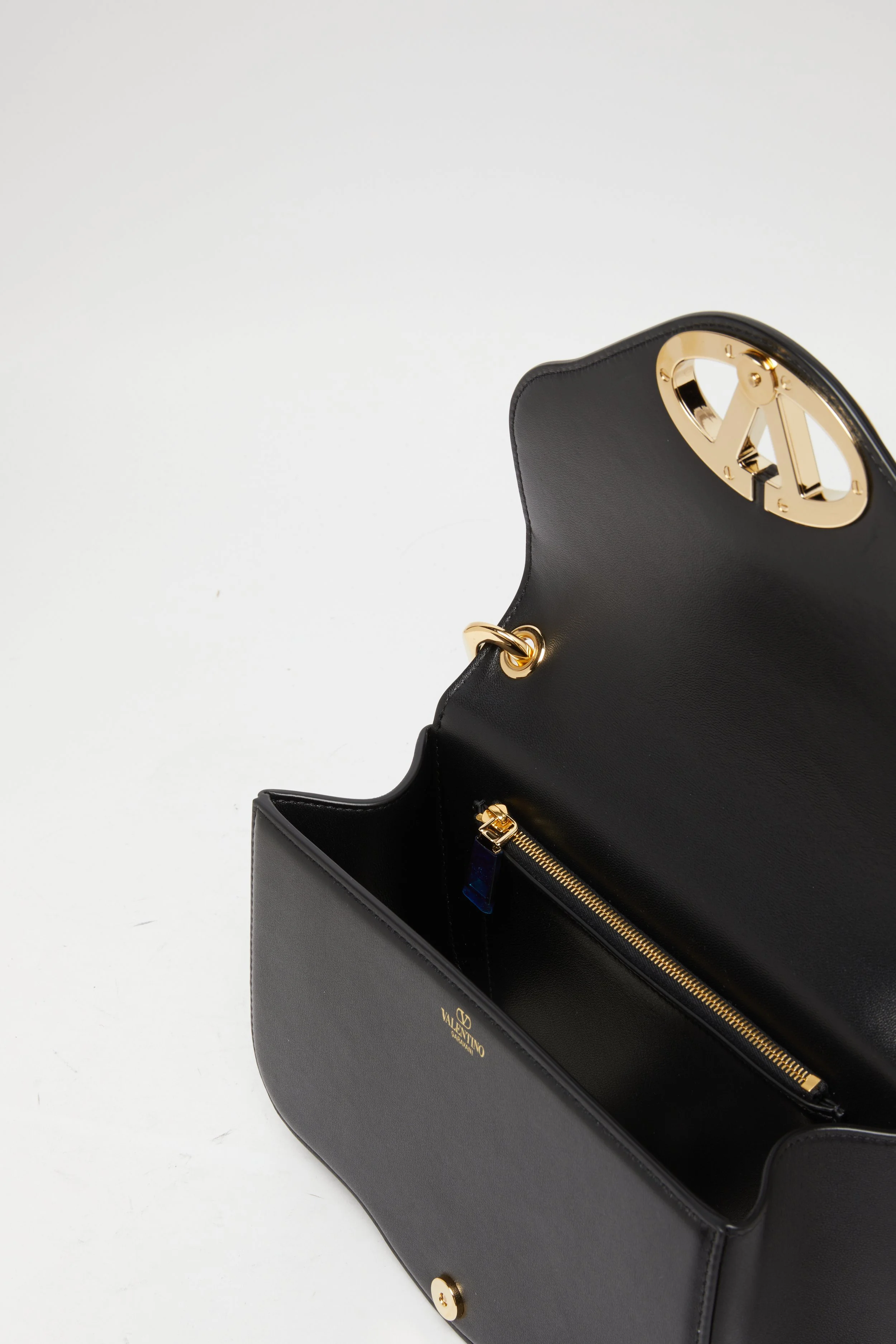 Sac à main noir avec intérieur en cuir, fermeture à glissière dorée et logo Valentino à l’intérieur.