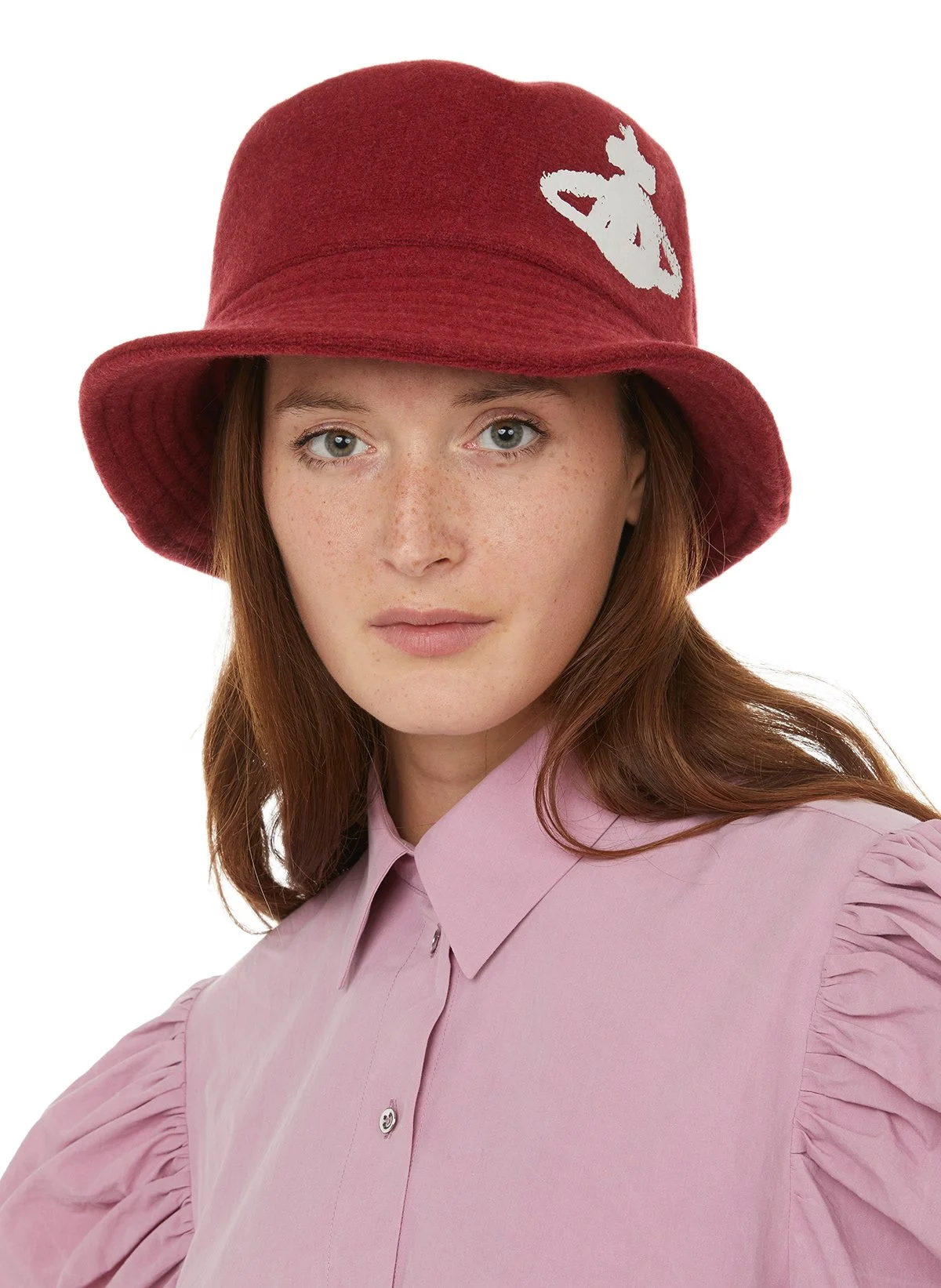 Jeune femme portant un chapeau rouge en feutre avec un motif blanc, chemise rose pâle à manches bouffantes.
