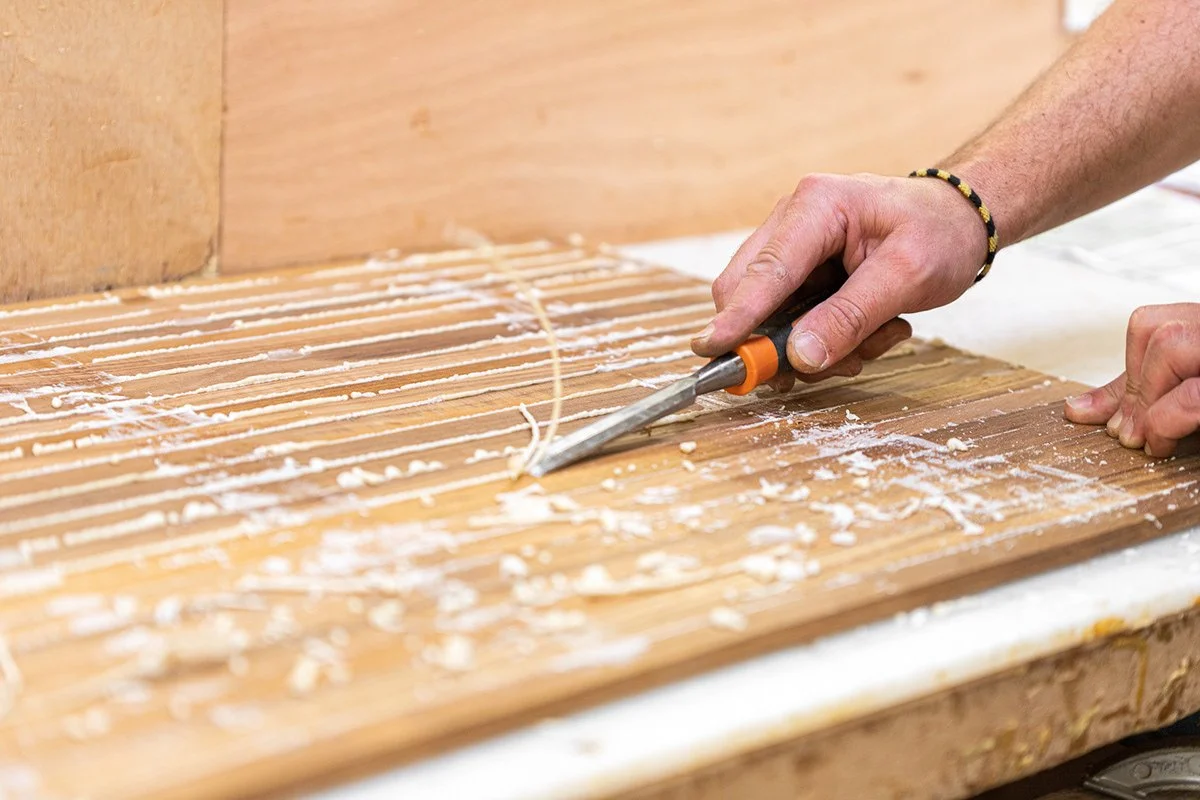 Une personne coupe des bandes de bois avec un cutter ou un outil de coupe sur une surface en bois, avec de la colle ou de la colle blanche visible sur le bois.