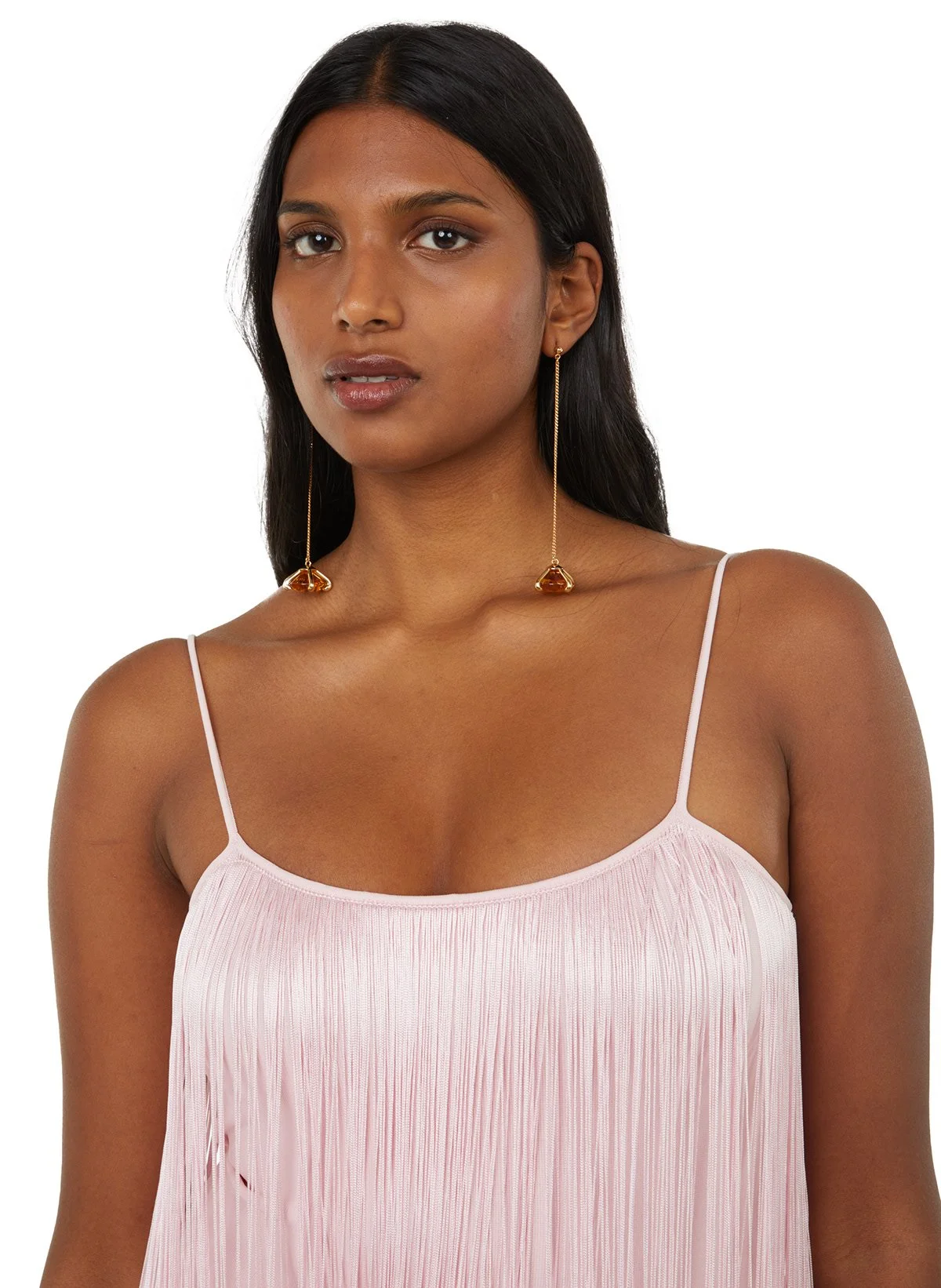 Femme portant un haut rose en tissu plissé et des boucles d'oreilles longues dorées avec pierre orange, cheveux noirs, peau foncée.