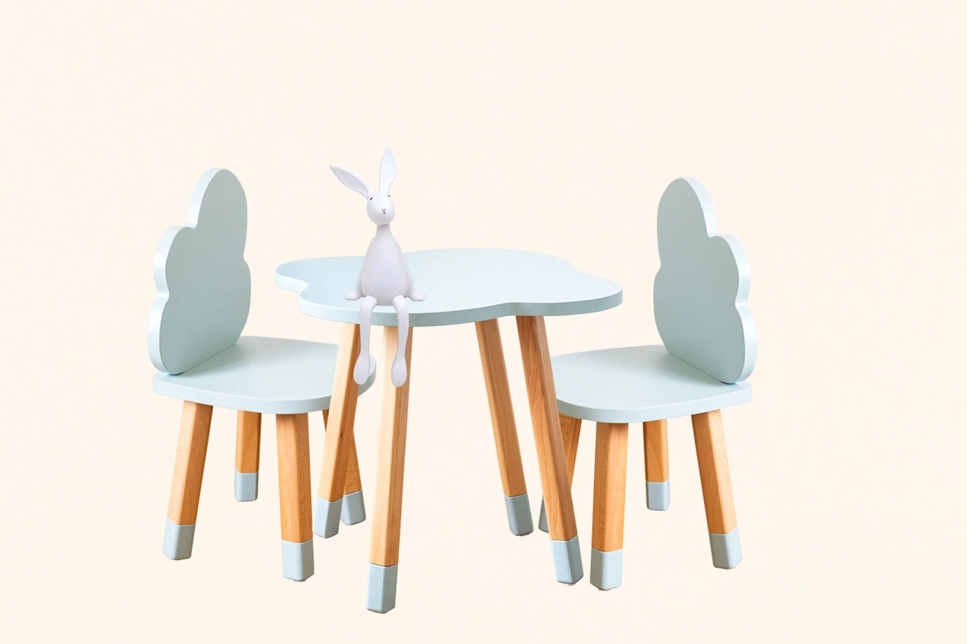 Un ensemble de meubles pour enfants comprenant une petite table ronde blanche avec deux chaises assorties, en bois clair avec des pieds gris, et une figurine de lapin blanc assise sur la table.