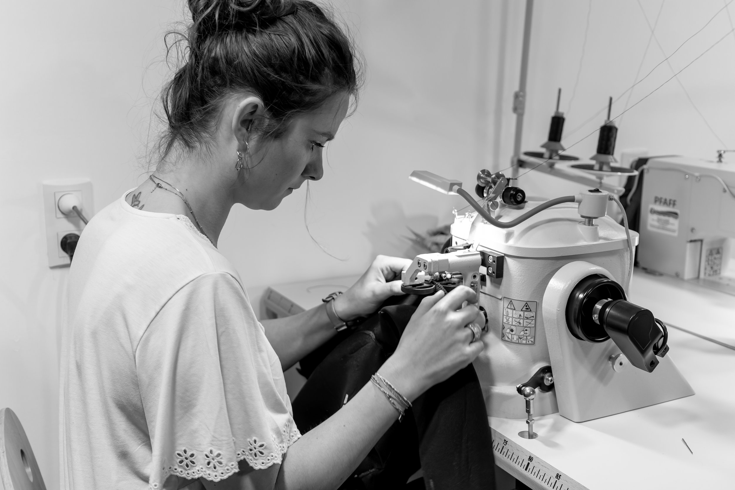 Femme travaillant sur une machine à coudre industrielle dans un atelier, en noir et blanc.