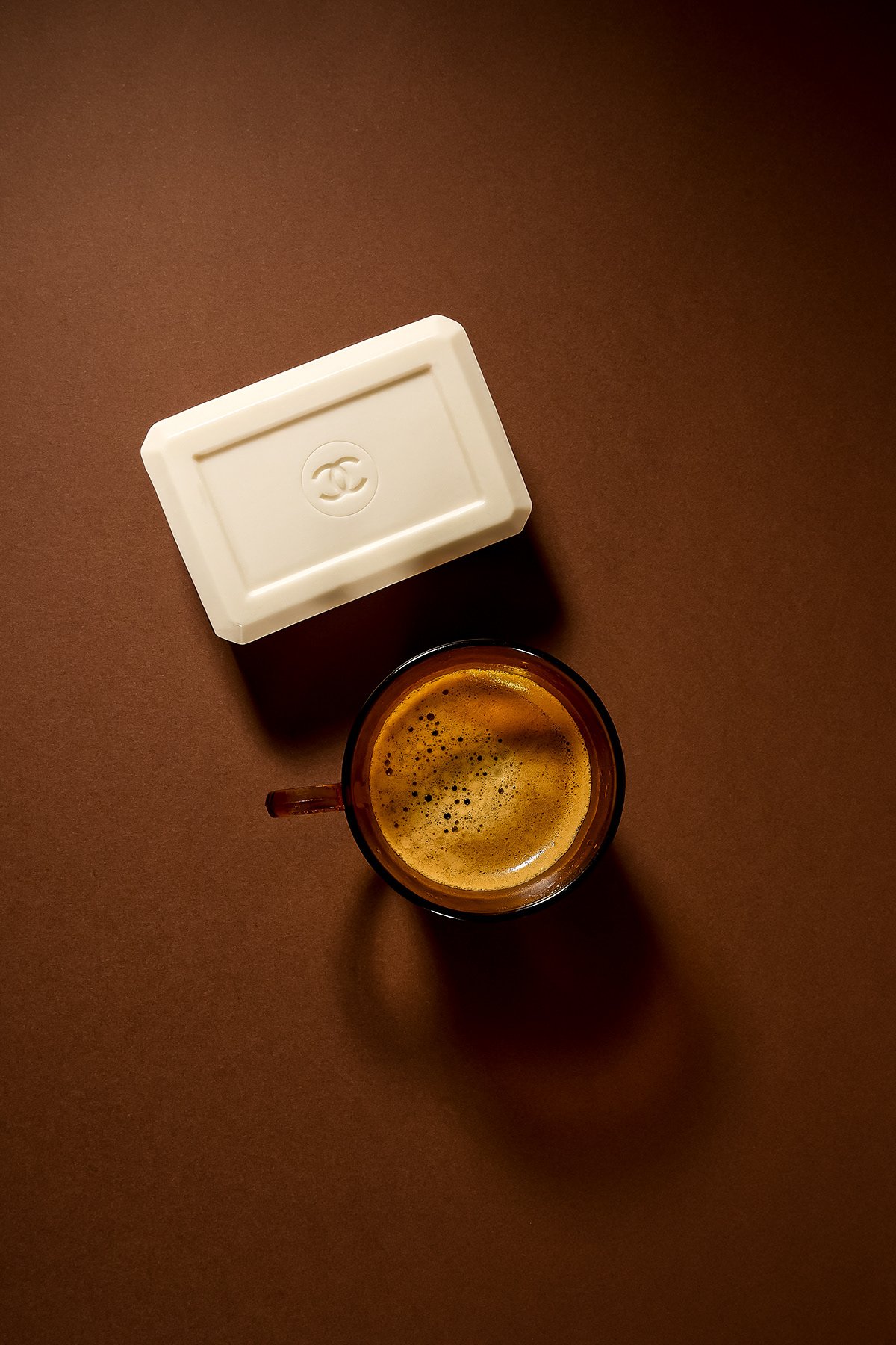 Tasse de café espresso avec mousse, placée sur une table marron, avec une boîte blanche à côté portant le logo de Chanel.