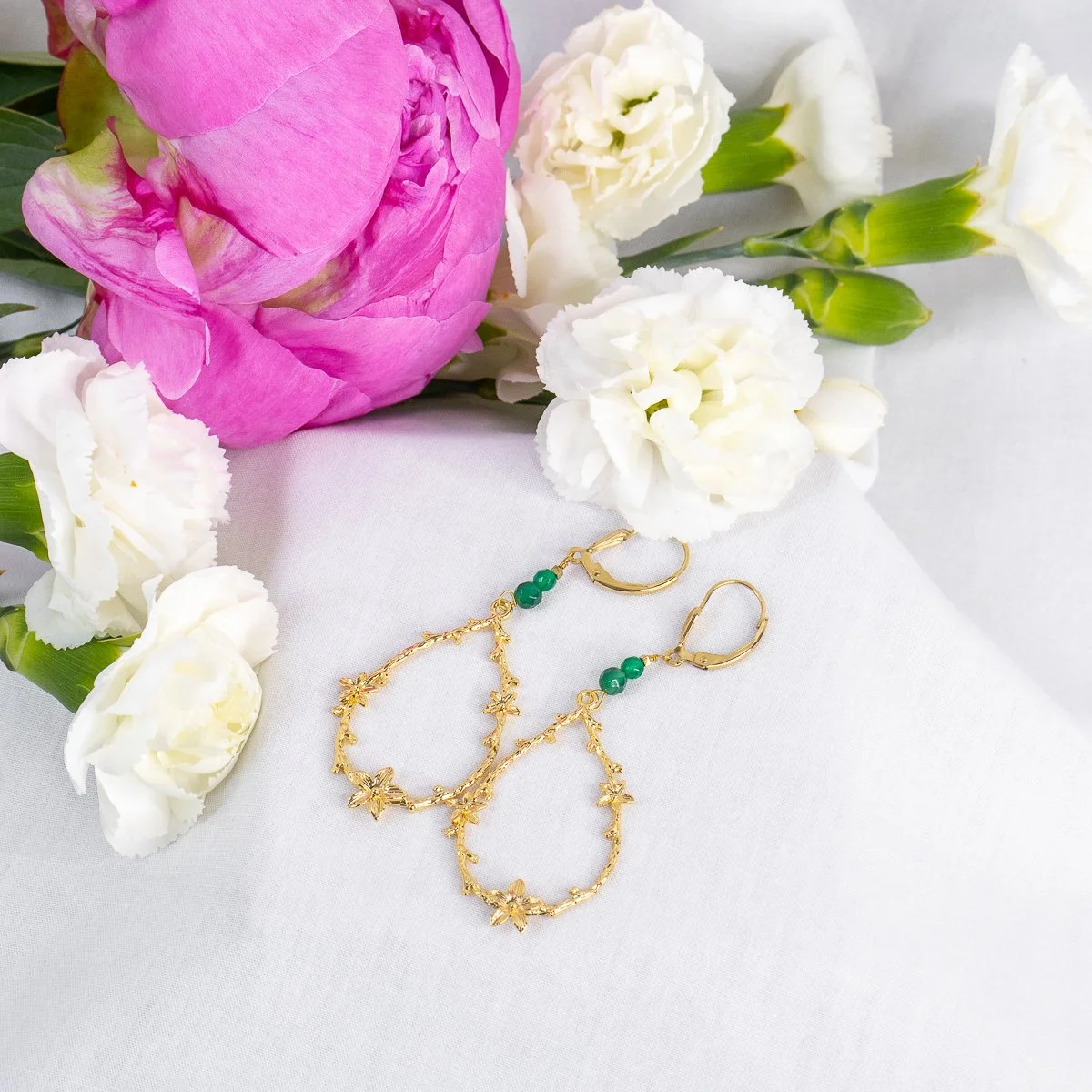 Bouquets de fleurs blanches et rose, avec deux boucles d'oreilles en or avec des perles vertes sur une surface blanche.