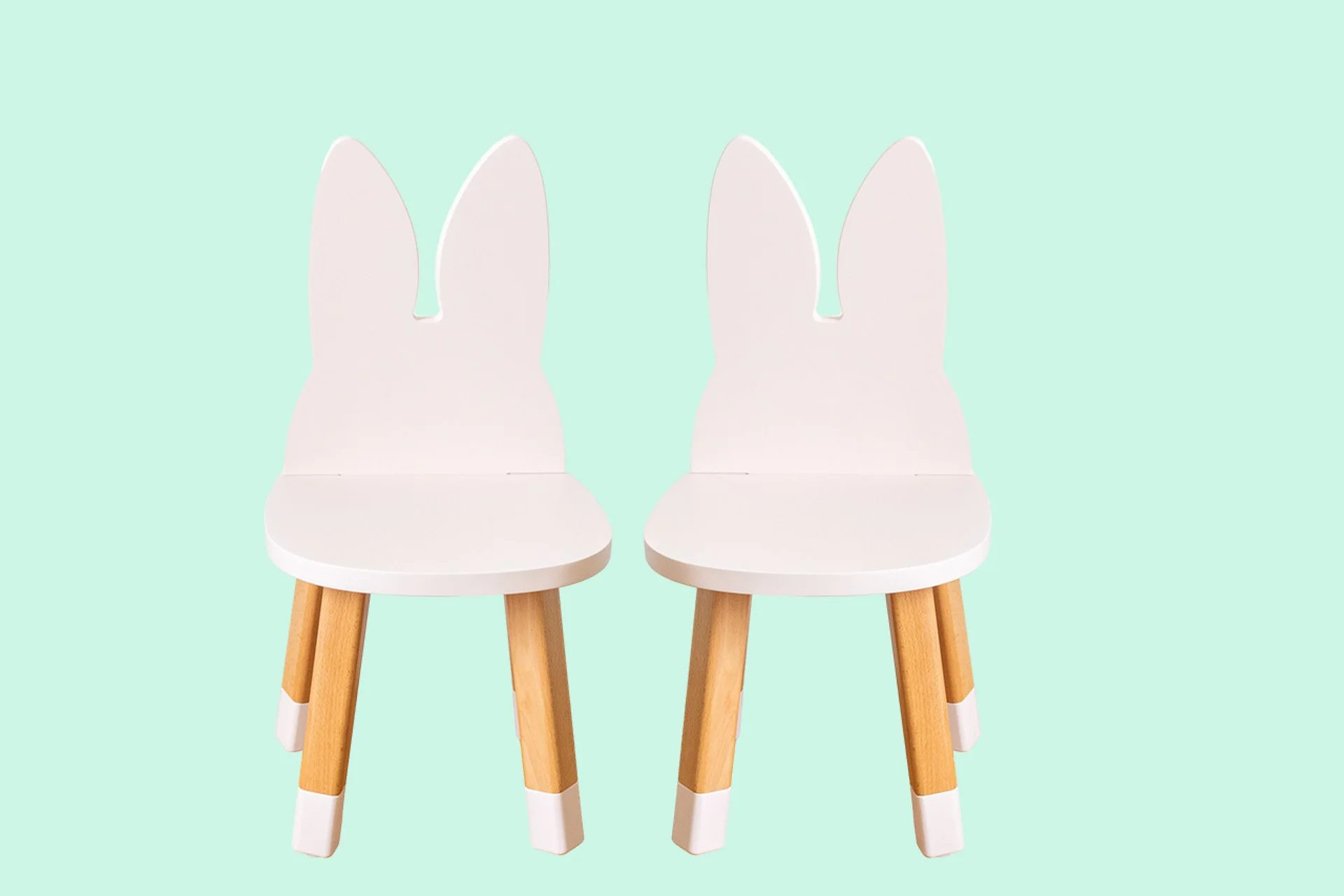 Deux chaises blanches en forme de lapin avec des oreilles en bois, sur un fond vert pastel.