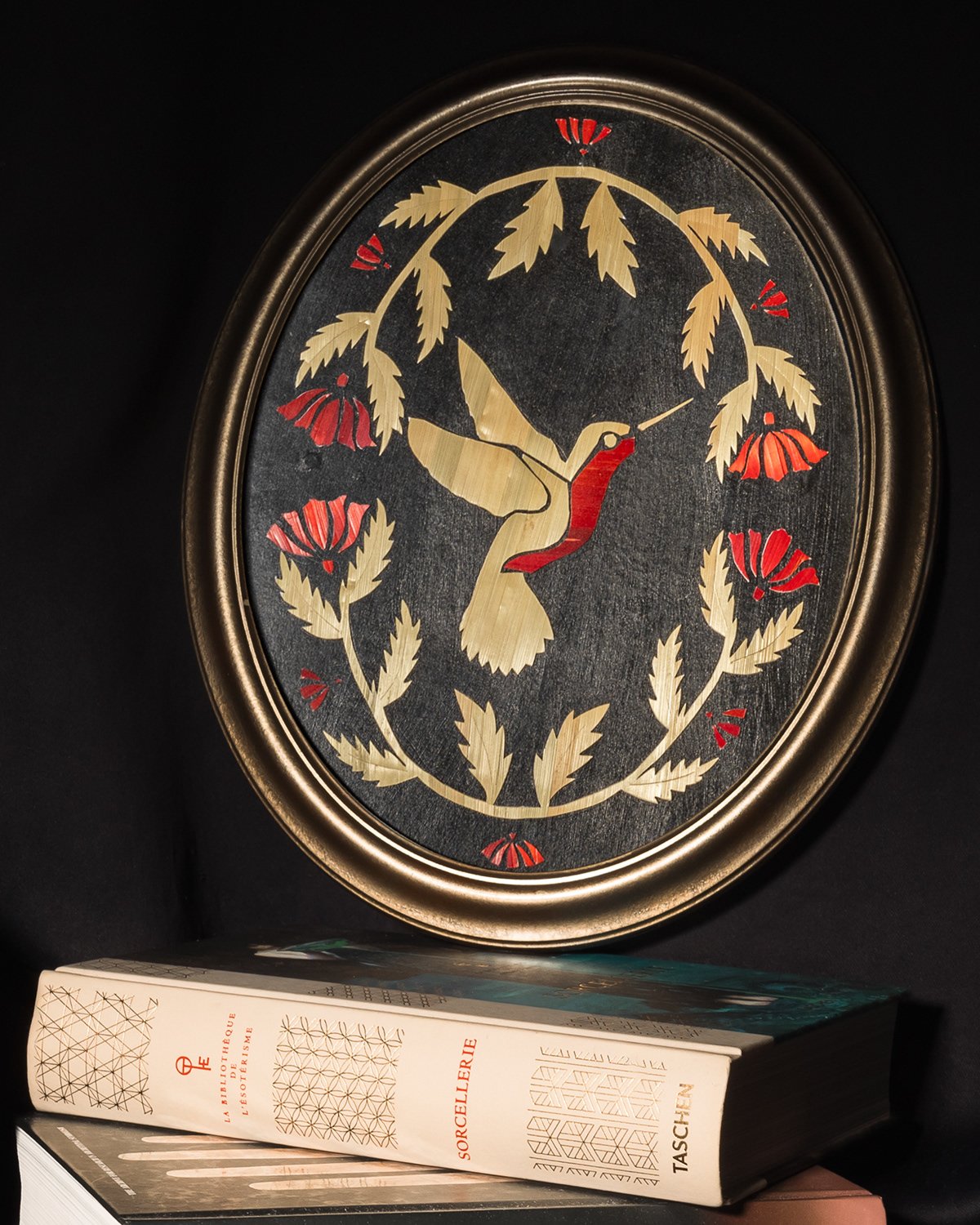 Horloge encadrée avec une illustration de colibri entouré de feuilles et de fleurs rouges, posé sur un livre épais.