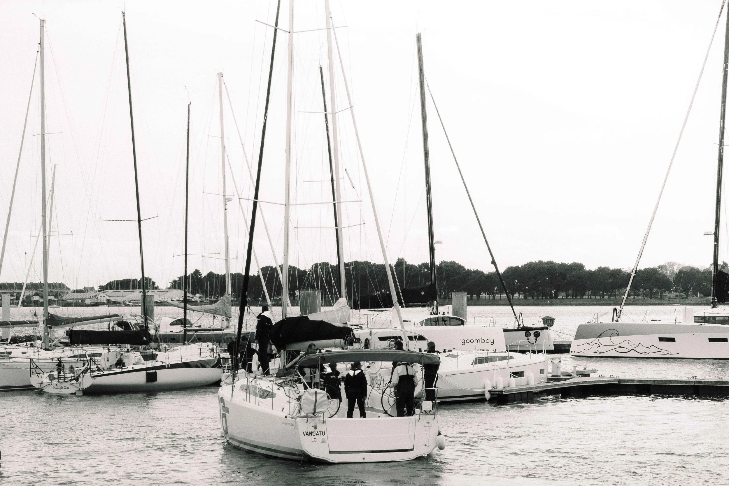 Bateaux à quai dans un port, plusieurs voiliers et yachts avec voiles ou sans voiles, quelques personnes sur un bateau