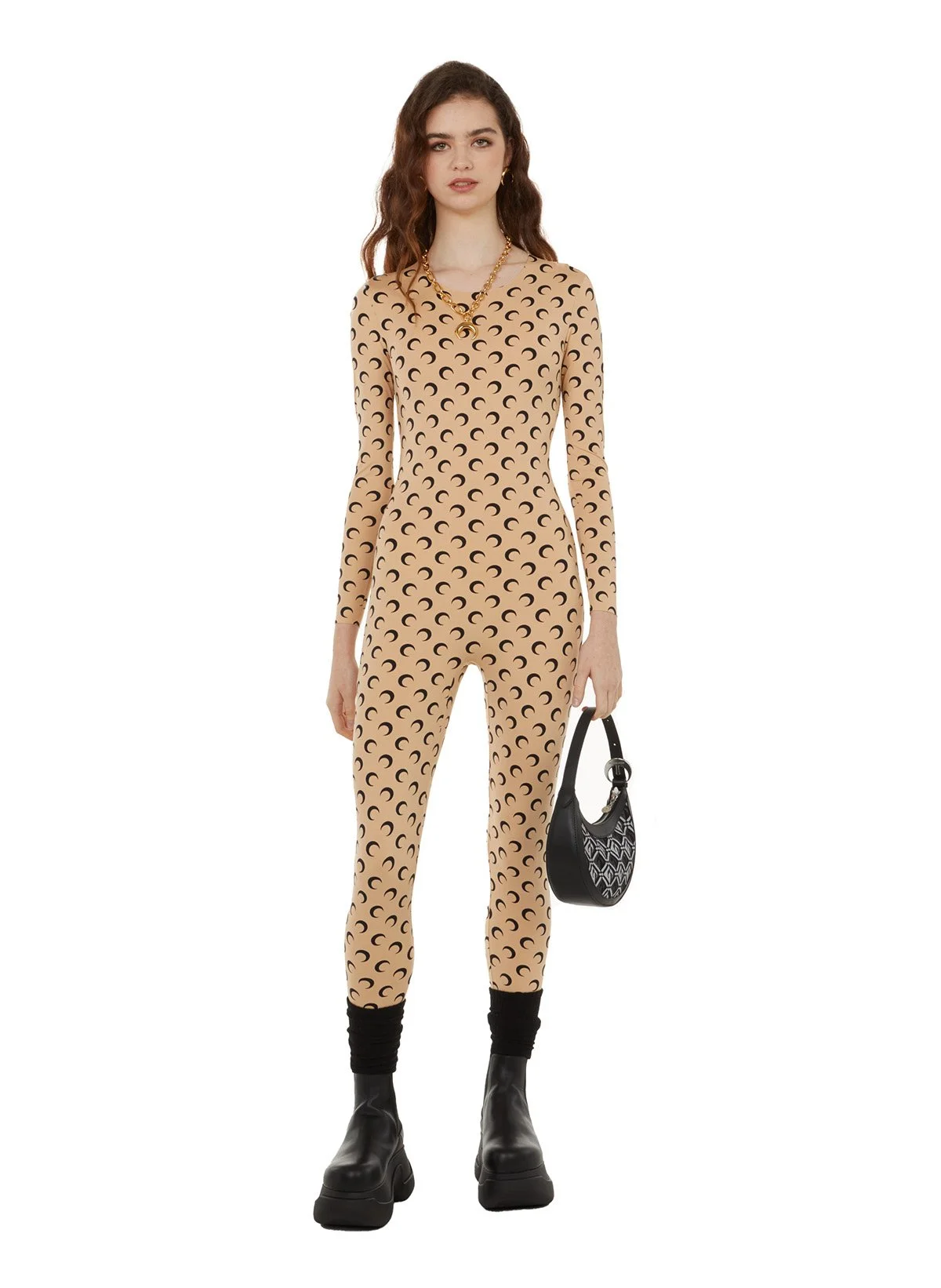 Femme portant un ensemble de mode beige avec motif de demi-lune, portant des chaussures noires épaisses, des bijoux dorés, et tenant un sac à main noir avec un motif blanc.
