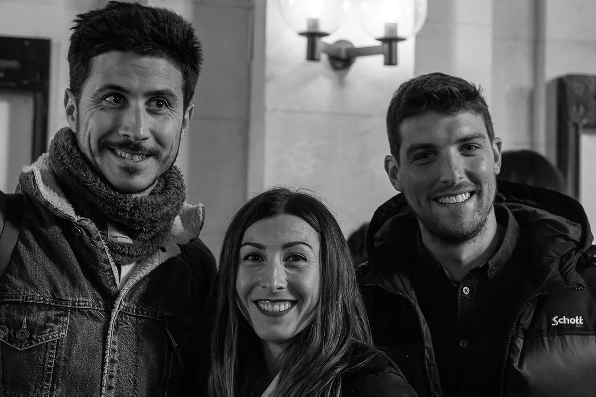 Trois personnes souriantes posant pour une photo dans un lieu intérieur, deux hommes et une femme.