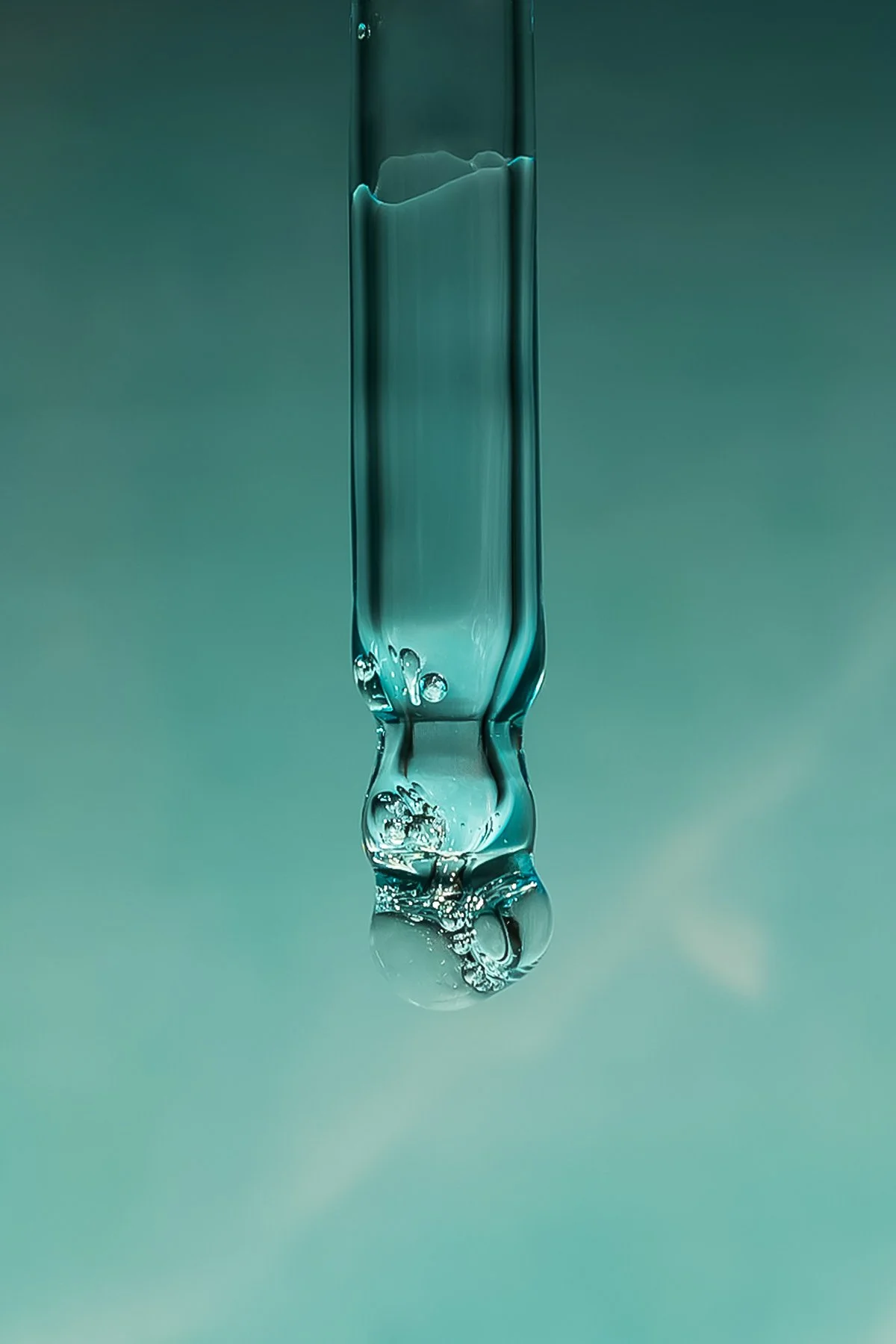 Une goutte d'eau suspendue au-dessus d'une surface, avec des bulles et des déformations dans l'eau, sur un fond vert pastel.