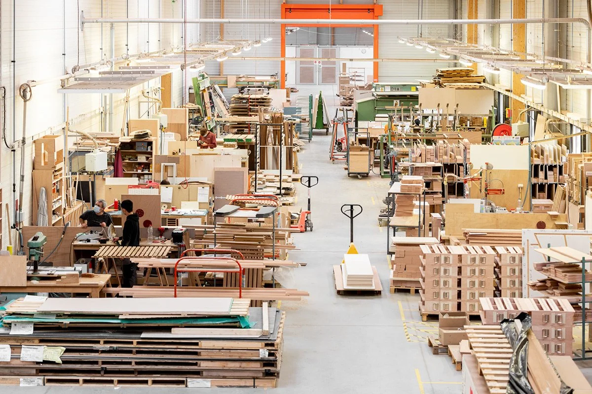 Une grande usine de fabrication de meubles en bois avec plusieurs travailleurs et piles de bois.