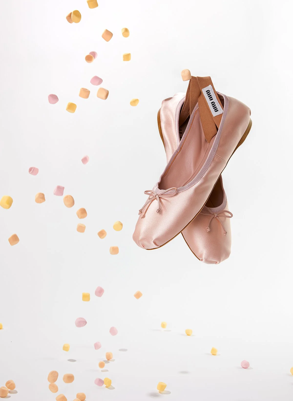 Des chaussons de ballet roses suspendus dans l'air avec des petits confettis pastel autour.