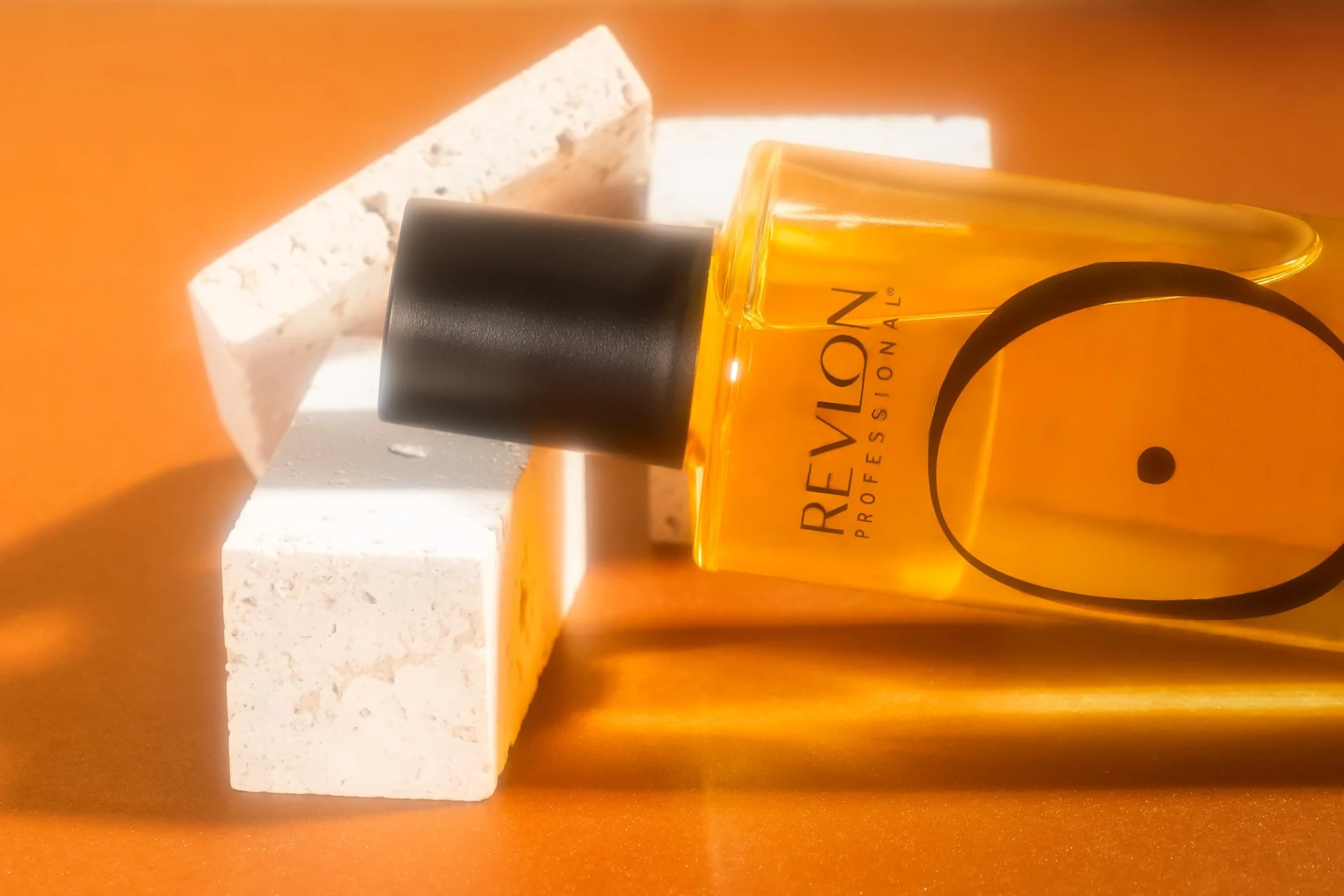 Une bouteille de parfum rougevion professionnel avec un bouchon noir, posée sur une surface orange, avec deux blocs de pierre blanche en arrière-plan.