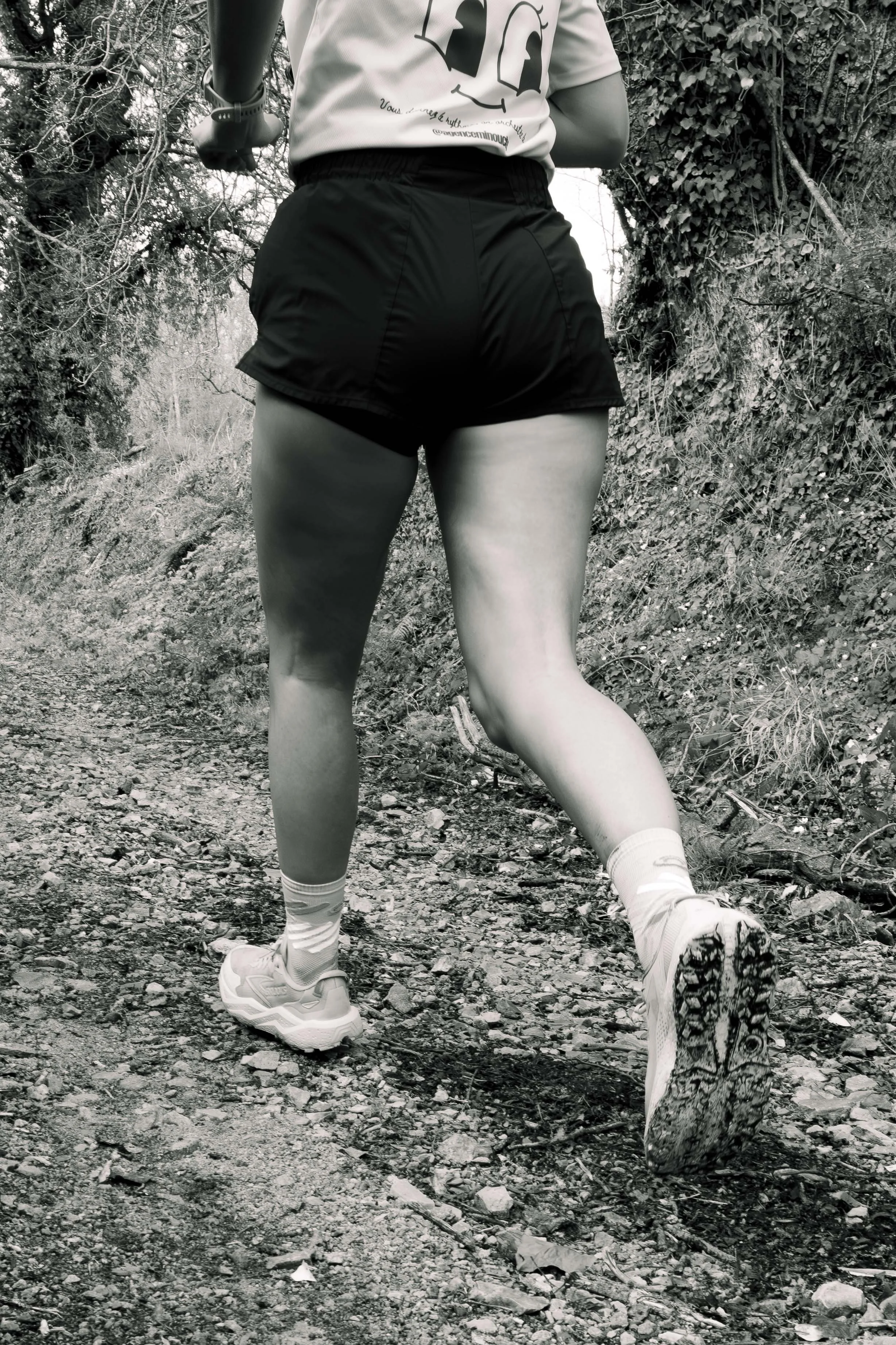 Une femme en chaussures de course, portant une jupe courte et un t-shirt, court sur un sentier boisé en forêt.